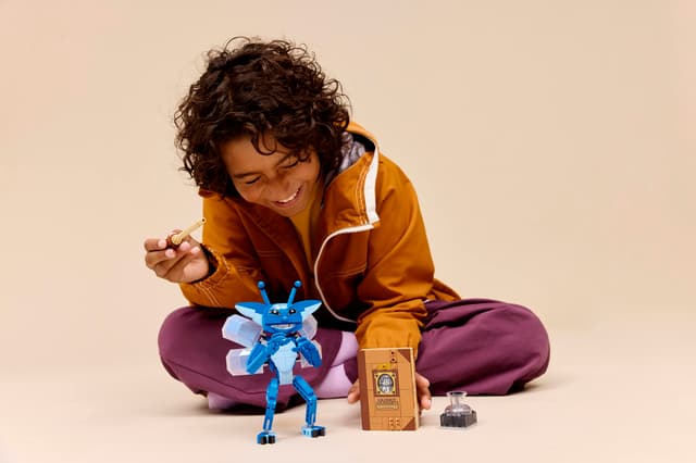 Child playing with a LEGO Harry Potter: Cornish Pixie blue toy figure and book on a beige background