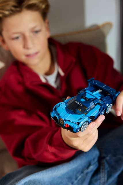 Child holding a blue LEGO Speed Champions: Bugatti Vision GT Hyper Sports Car indoors