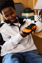 Child holding a LEGO Speed Champions: McLaren W1 in a room with books and a lamp in the background