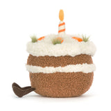 Soft plush toy designed as a whimsical cake with white fluffy frosting, orange carrot decorations, a striped candle on top, and small brown legs, called Amuseables Carrot Cake.