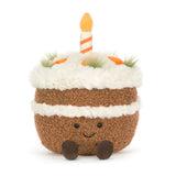 Soft plush Amuseables Carrot Cake toy with white frosting, orange carrot decorations, a striped candle on top, and a smiling face with small brown feet.