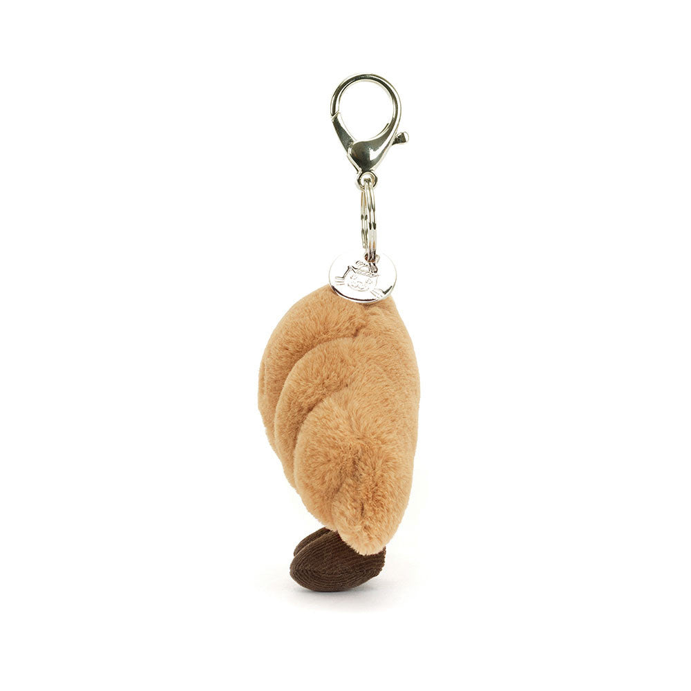 Side view of a plush Amuseables Croissant Bag Charm on a white background