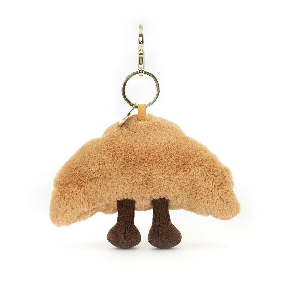 Rear view of a plush Amuseables Croissant Bag Charm with legs on a white background