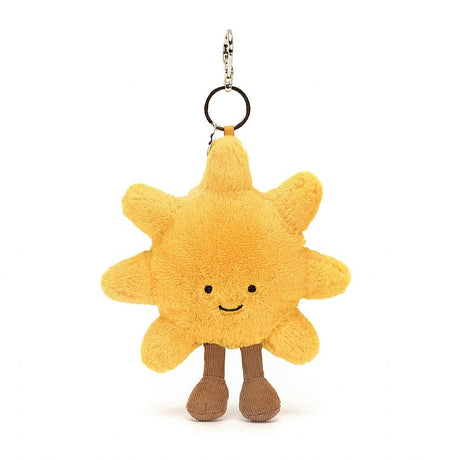 Amuseables Sun Bag Charm featuring a soft yellow sun plush with a smiling face and brown legs, designed as a playful accessory for bags or backpacks.