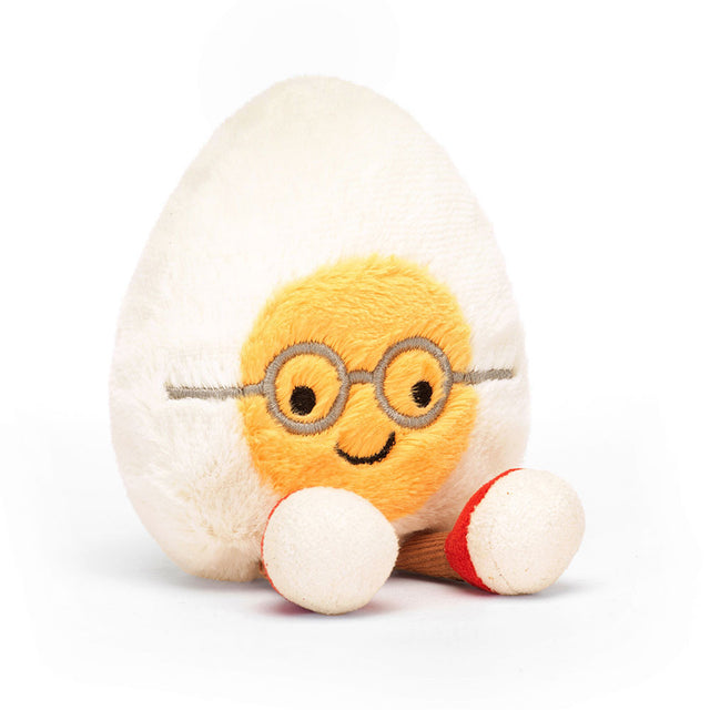 Soft plush toy shaped like a smiling boiled egg with glasses and small legs wearing red and white shoes, called Amuseables Boiled Egg Geek.