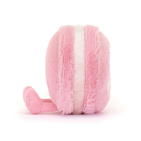 Side view of a soft pink plush toy shaped like a macaron with a textured, lighter pink filling and a small corduroy feet, named Amuseables Mia Macaron.
