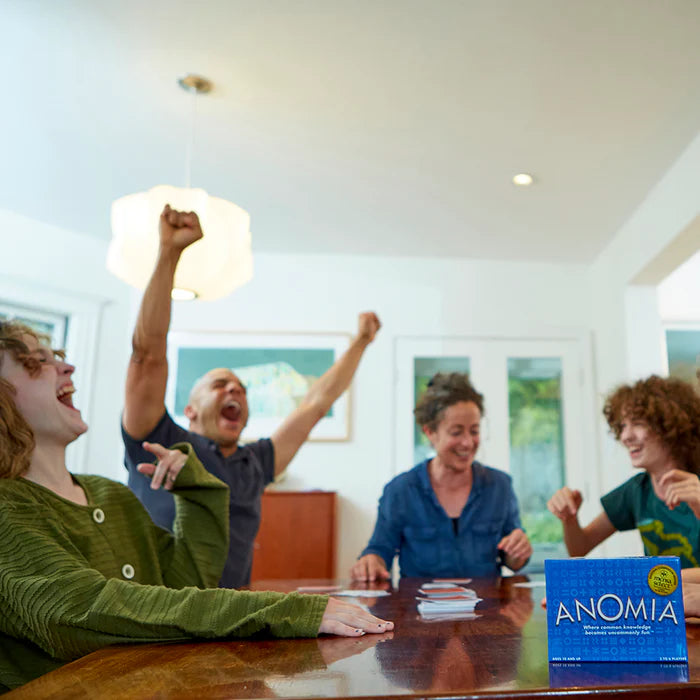 People playing a board game together with 'ANOMIA' box on a table.