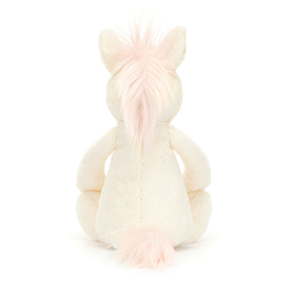 Bashful Unicorn Medium plush toy sitting with its back visible, featuring soft cream fur and light pink mane and tail, perfect as a kid’s birthday gift or stuffed animal.