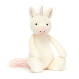 Bashful Unicorn Medium plush toy with a soft cream-colored body, light pink accents on the snout and tail, and a shiny silver horn, sitting upright on a white background.