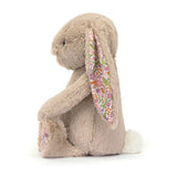 Side view of a plush Blossom Beige Bunny 'Petal' toy with floral ear on a white background