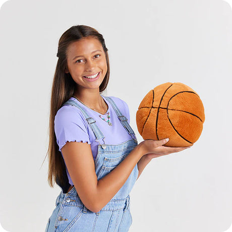 Young girl holding a plush Basketball Warmies against a plain background