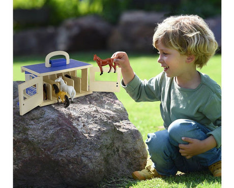 Child playing with a toy horse stable and figurines outdoors
