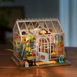 Rolife Dreamy Garden House DIY Miniature House Kit model of a greenhouse with plants and furniture on a wooden surface.