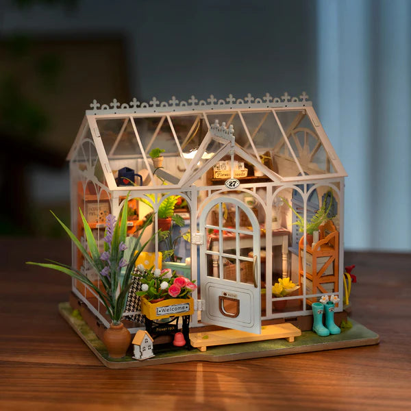 Rolife Dreamy Garden House DIY Miniature House Kit model of a greenhouse with plants and furniture on a wooden surface.