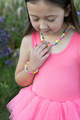 Young girl in a pink dress wearing colorful Fruity Tooty Bracelet outdoors.