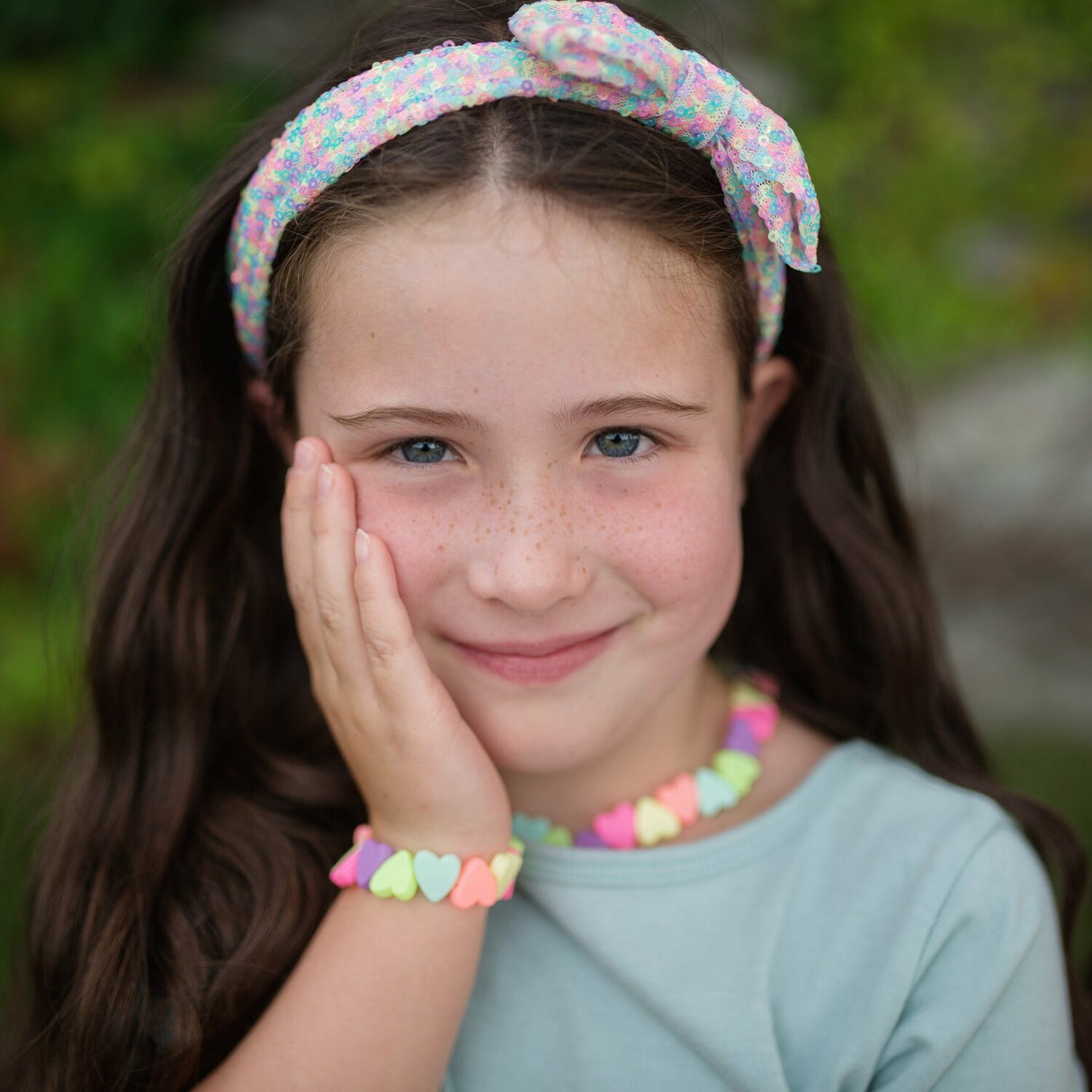 Young girl wearing colorful headband and Sweet Tart Heart Necklace & Bracelet Set with a blurred green background
