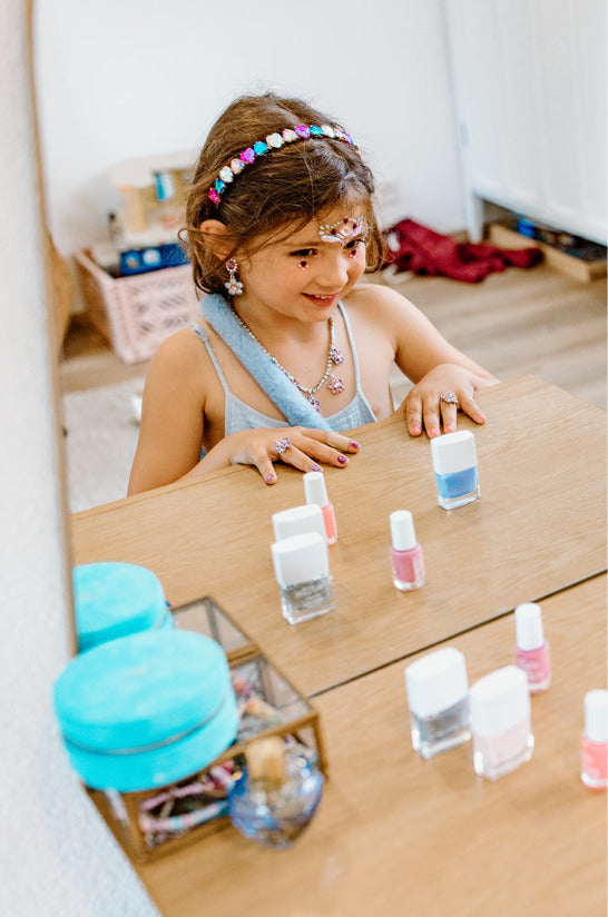 Young girl wearing a Boutique Heartbreaker Headband  and playing with miniature nail polish bottles on a wooden surface.