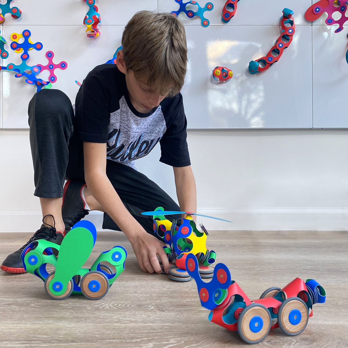 Child playing with colorful Wheel Creator Pack on a wooden floor.