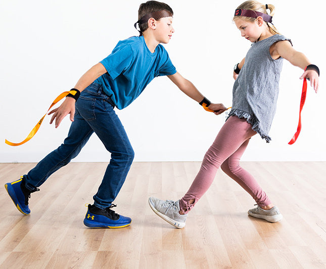 Two children playing Ribbon Ninja Game on a wooden floor.