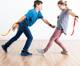 Two children playing Ribbon Ninja Game on a wooden floor.