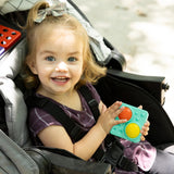 Child in a stroller holding a colorful PlayTab Tiles Set 4 , smiling outdoors.