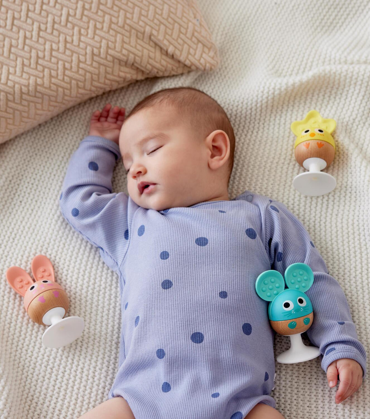 Baby lying on a textured surface with colorful Cheery Critter Rattle Trio around