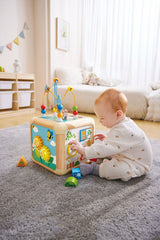 Baby playing with a colorful Green Thumbs Activity Cube on a carpeted floor.