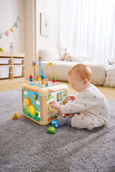 Baby playing with a colorful Green Thumbs Activity Cube on a carpeted floor.
