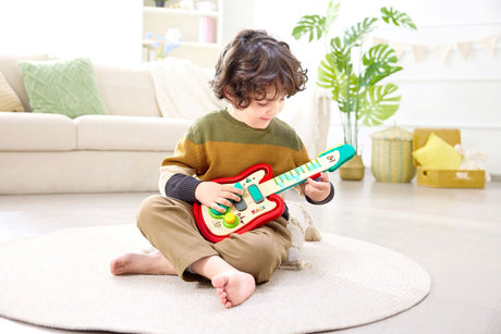Child playing with a colorful toy Rainbow Rock Guitar (Pixelz) in a living room setting.