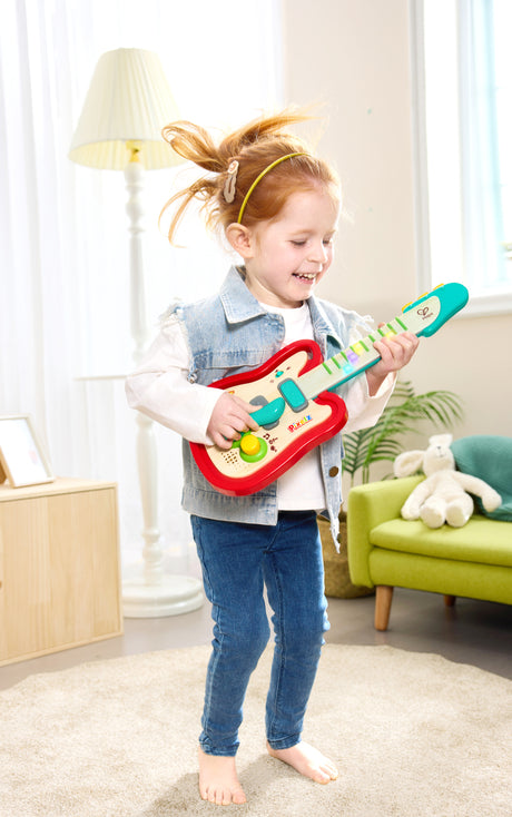 Child playing with a toy Rainbow Rock Guitar (Pixelz) in a bright living room