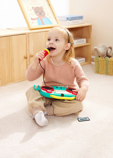 Child playing with a toy Sing-Along Pixel Boombox (Pixelz) in a room with wooden furniture.
