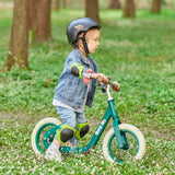Child riding a green balance bike in a grassy area with trees in the background