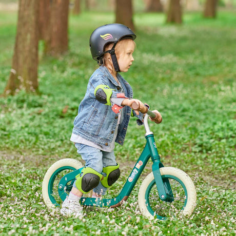 Child riding a green balance bike in a grassy area with trees in the background