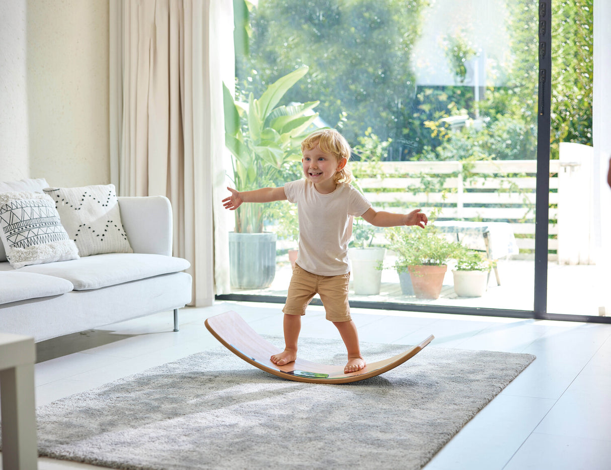 Child balancing on a Light-Up Balance Board in a modern living room with large windows.