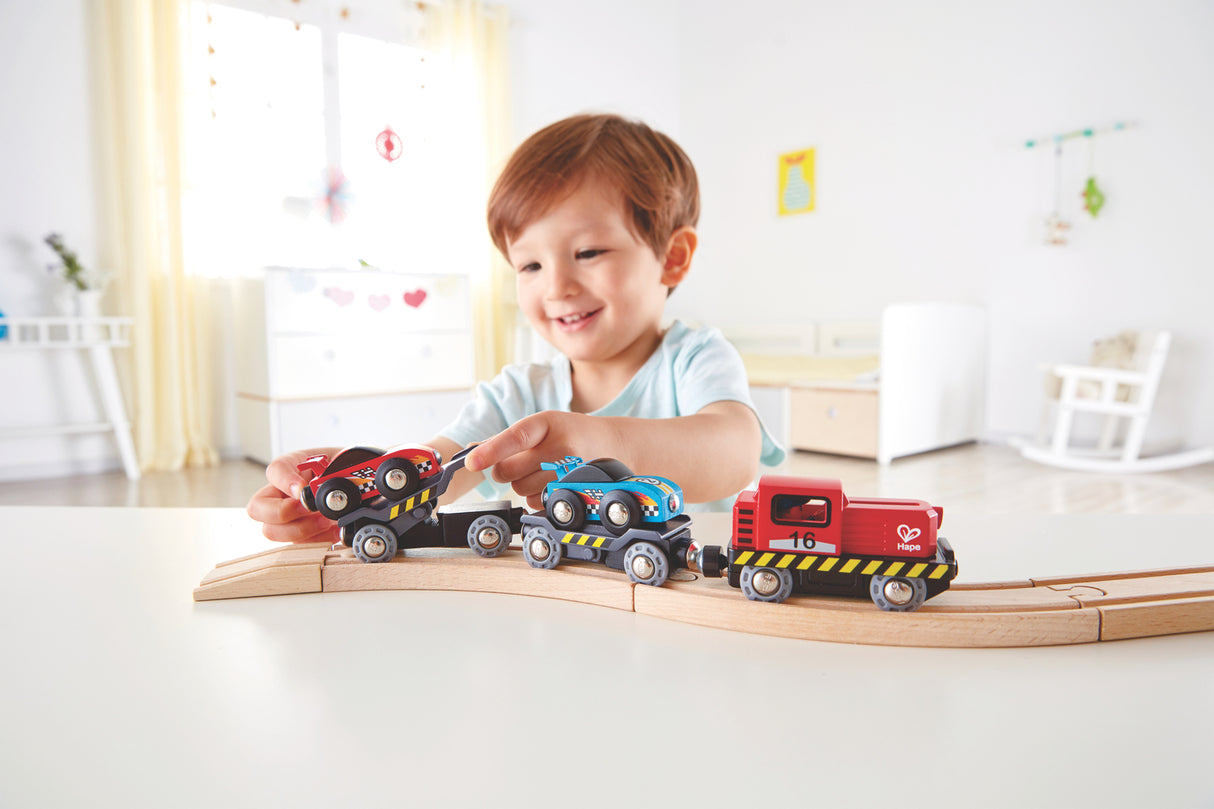 Child playing with toy Race Car Transporter on a wooden track in a bright room