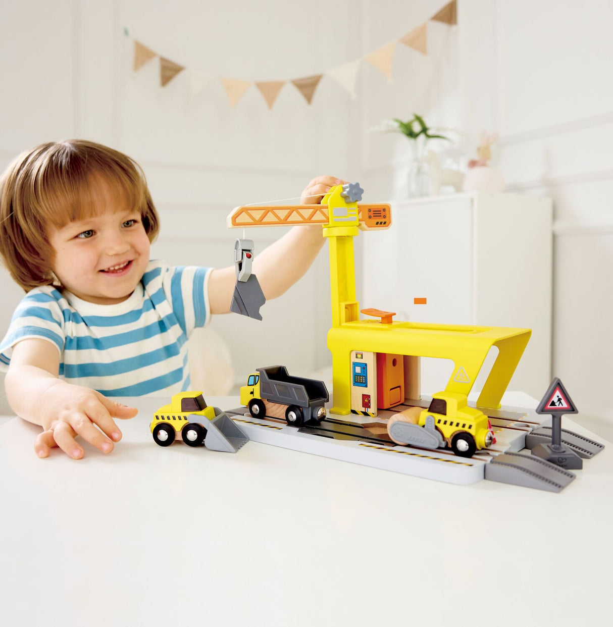 Child playing with a toy Railway Crane Construction set on a white surface