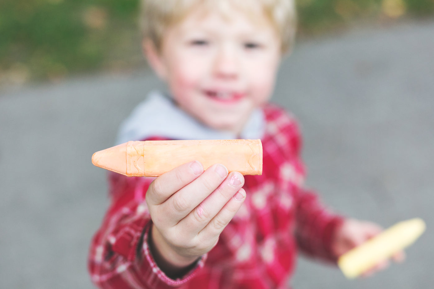 Child in red jacket holding orange chalk.