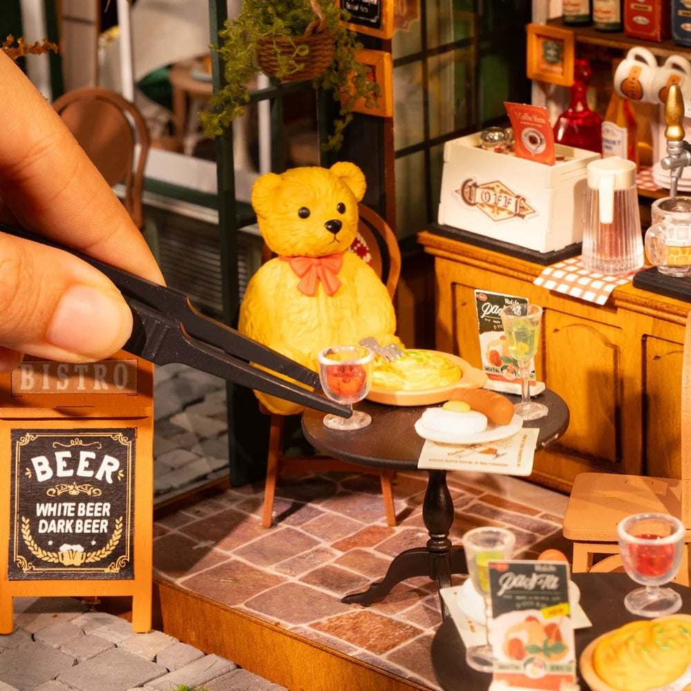 Tipsy Restaurant DIY Miniature House with miniature teddy bear sitting at a table with a drink and food in a bistro setting.