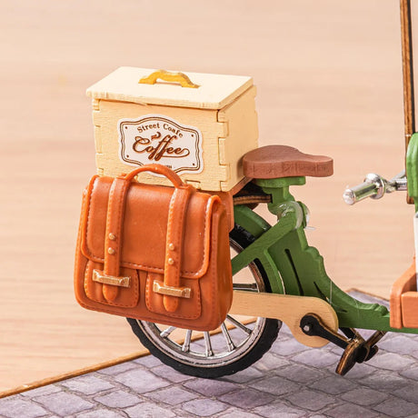 Toy bike with a wooden box labeled 'Street Coffee' and a brown leather bag on a beige background included with the e Aromatic Coffee Cart kit.