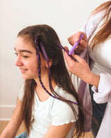 Person coloring a girl's hair with purple Hair Doodlers Hair Crayon against a white background