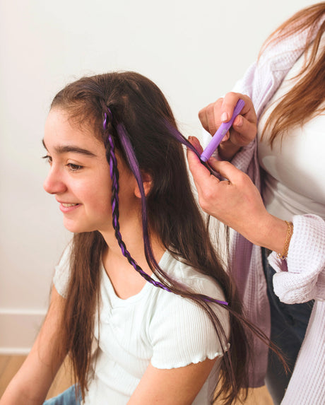 Person coloring a girl's hair with purple Hair Doodlers Hair Crayon against a white background