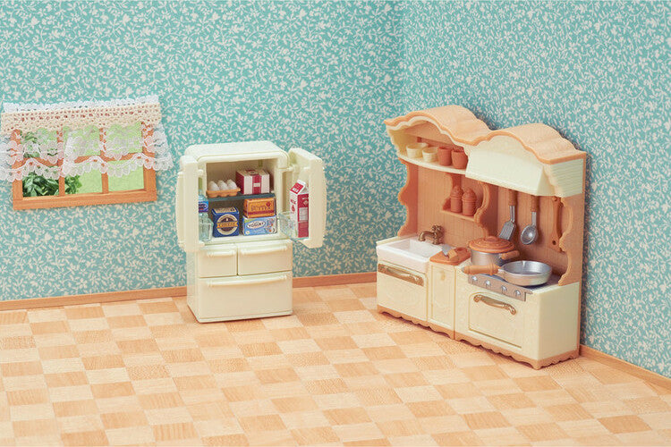 Toy Calico Critters kitchen play set  with refrigerator and cabinets against a patterned wall.