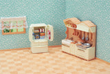 Toy Calico Critters kitchen play set  with refrigerator and cabinets against a patterned wall.