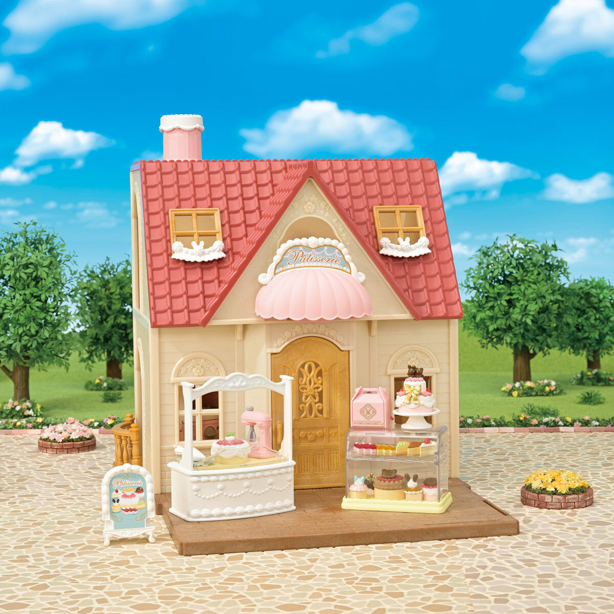 Toy Calico Critters - Village Cake Shop Starter Set with a pink roof and various display cases against a blue sky.