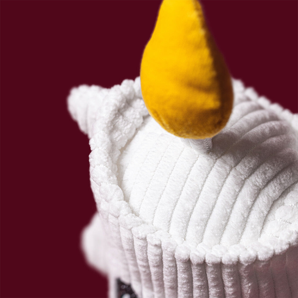 A close-up of a white Amuseables Flickerty Candle plush toy set against a solid dark red background.
