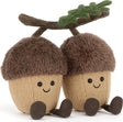 Two plush Amuseables Ort & Tum Acorns with brown fuzzy caps, beige textured bodies, embroidered smiling faces, and small brown feet, attached to a brown branch with green leaves on a white background.