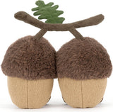 A pair of plushAmuseables Ort & Tum Acorns with fuzzy brown caps, beige textured bodies, and a brown branch with a green leaf on top, shown on a plain white background.