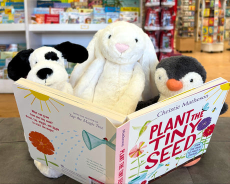 Plush toys in front of a book titled 'Plant the Tiny Seed' in a bookstore setting.