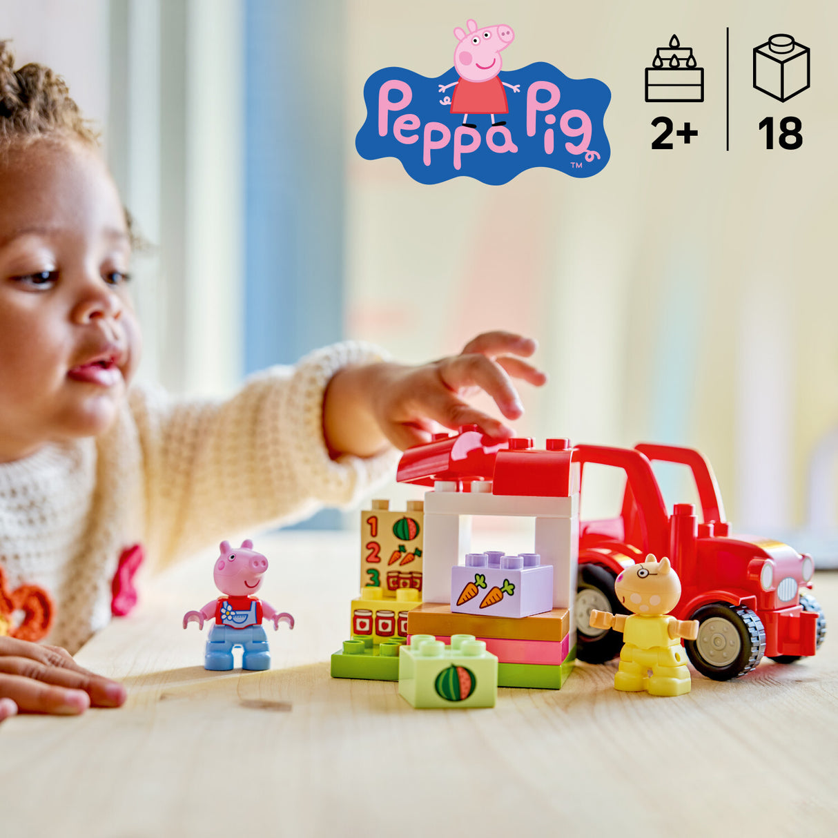 Child playing with LEGO DUPLO Peppa Pig: Tractor and Market toy set on a light surface, with Peppa Pig logo visible.