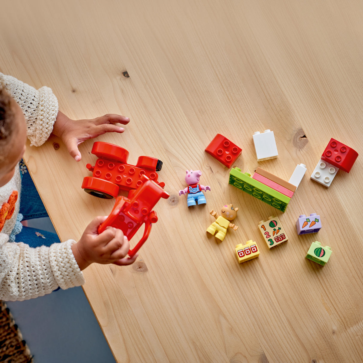 Child playing with colorful LEGO DUPLO Peppa Pig: Tractor and Market building blocks on a wooden floor